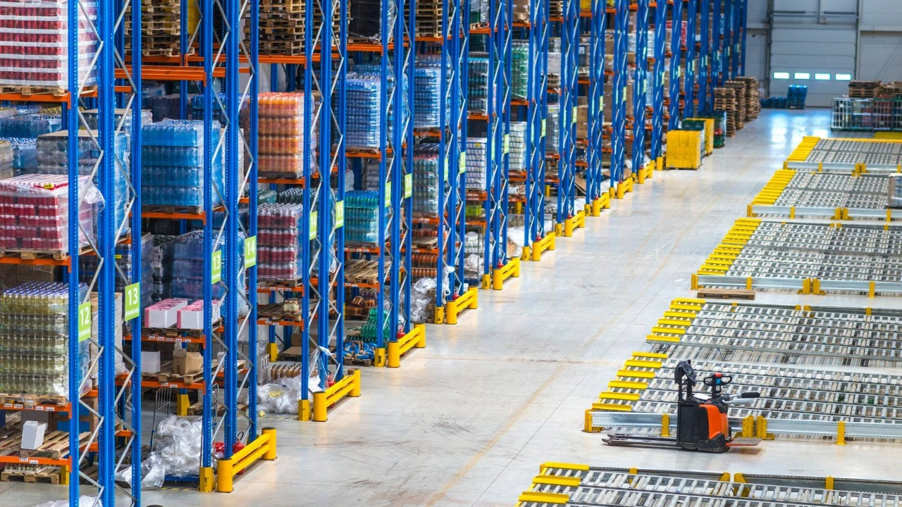 Un magazzino con scaffalature blu cariche di merce su pallet e un transpallet elettrico nella corsia