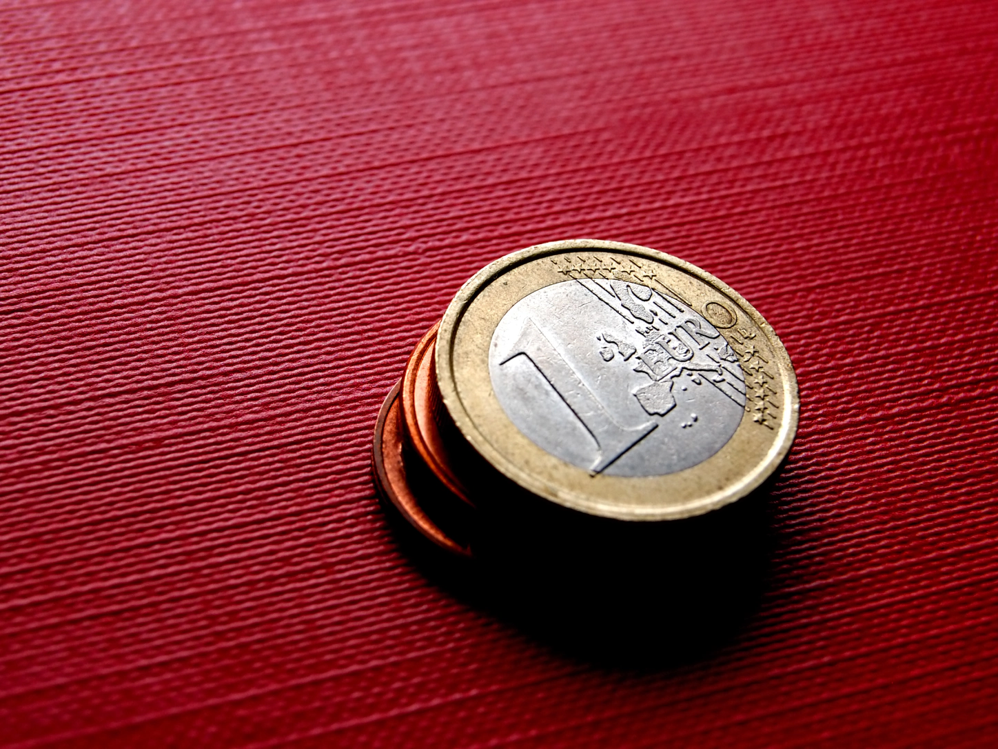 Una moneta da un euro sopra alcune monetine, su una superficie rossa
